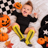 Yellow lace-up print socks worn with black bodysuit among pumpkins